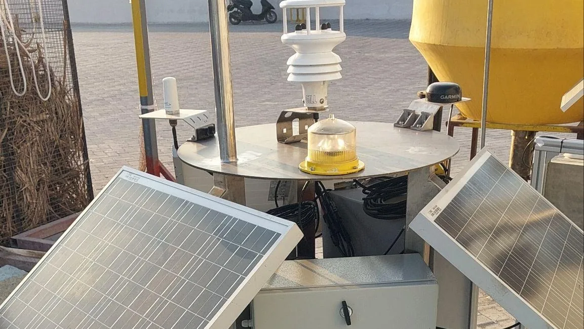 Marine buoy deck during construction with weather station, navigation light and solar panels, with the yellow hull behind
